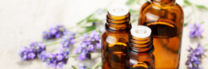 Small, opened lavender essential oil bottles, ready to be used on the skin for sleep with fresh lavender flower heads next to them.
