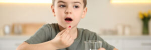 Little boy with glass of water taking vitamin capsule in kitchen