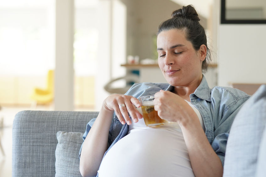 Pregnant woman relaxing in sofa drinking hot herbal tea