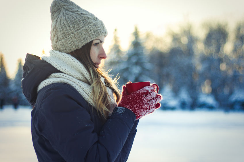 Young Girl in Red Gloves holds a Red Cup with Hot Tea on the Winter Landscape Background with Sunset