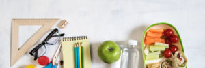 A pile of various stationery on table, notepad, colored pencils, ruler, marker, planer, space for text. Delicious school lunch box, sandwich and fruit. The concept of preparing children