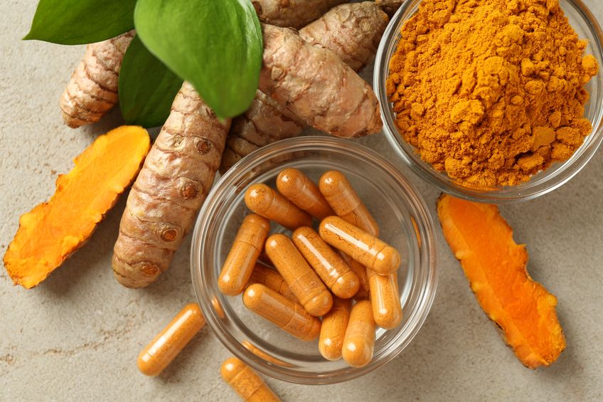 Turmeric capsules, powder, roots and green leaves on grey table, flat lay