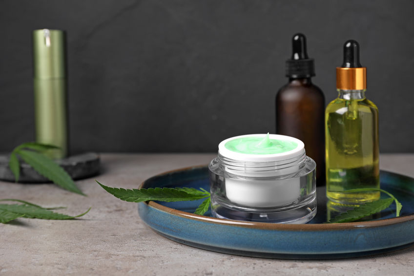 CBD cosmetics and green leaves on light grey table