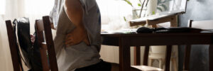 Working woman sitting on the chair in the living room at home She used both hands to press down on the lower back. She is suffering from back pain from sitting for a long time.