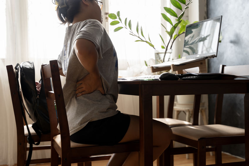 Working woman sitting on the chair in the living room at home She used both hands to press down on the lower back. She is suffering from back pain from sitting for a long time.