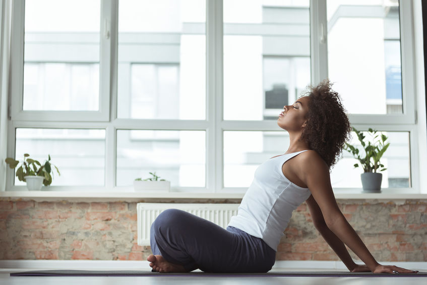 Side view serene girl doing exercise on mat in cozy room. She sitting on floor
