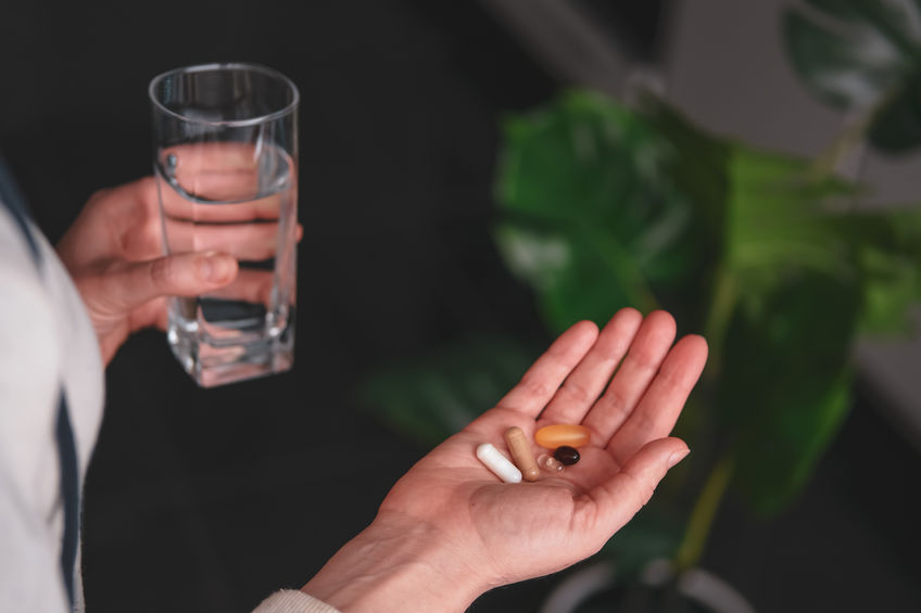 Woman's hand with a pile of various pills and a glass of water. Nutrition supplements and health care concept.
