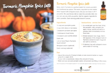 Two mugs of turmeric pumpkin spice latte sit on a table, accompanied by a recipe card and small pumpkins in the background.